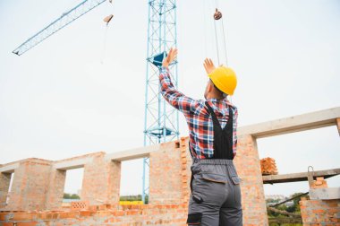 Vinçli adamla iletişim kuruyorum. Üniformalı inşaat işçisi ve güvenlik ekipmanı inşaatında çalışıyor