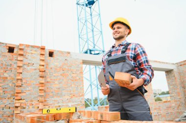 Tuğla duvarla meşgul. Üniformalı inşaat işçisi ve güvenlik ekipmanı inşaatında çalışıyor