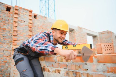 Tuğla kullanarak. Üniformalı genç inşaat işçisi tamamlanmamış binada meşgul..