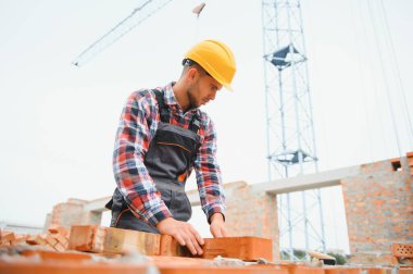 Sarı renkli başlık. Gündüz vakti inşaatta üniformalı genç bir adam çalışıyor.