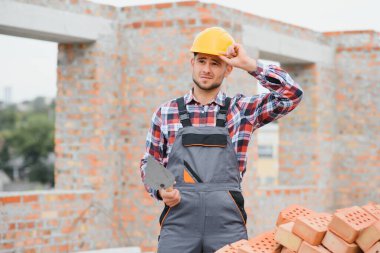 Sarı renkli başlık. Gündüz vakti inşaatta üniformalı genç bir adam çalışıyor.