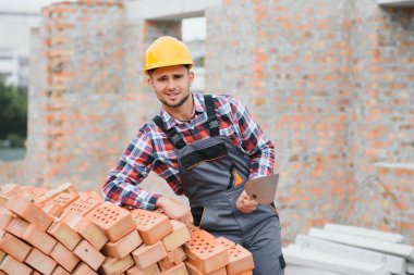 Sarı renkli başlık. Gündüz vakti inşaatta üniformalı genç bir adam çalışıyor.