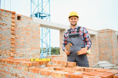 Construction worker man in work clothes and a construction helmet. Portrait of positive male builder in hardhat working at construction site