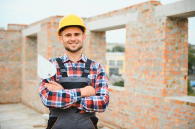 Construction worker man in work clothes and a construction helmet. Portrait of positive male builder in hardhat working at construction site