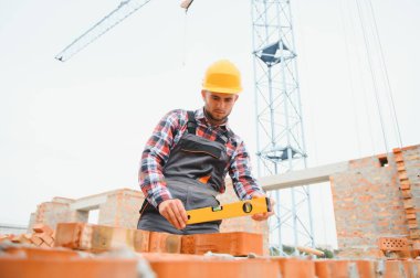 Tuğla kullanarak. Üniformalı genç inşaat işçisi tamamlanmamış binada meşgul..