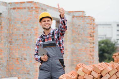 Sarı renkli başlık. Gündüz vakti inşaatta üniformalı genç bir adam çalışıyor.