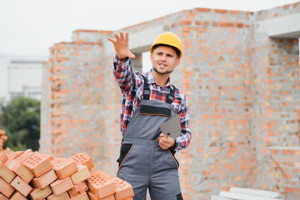 Sarı renkli başlık. Gündüz vakti inşaatta üniformalı genç bir adam çalışıyor.