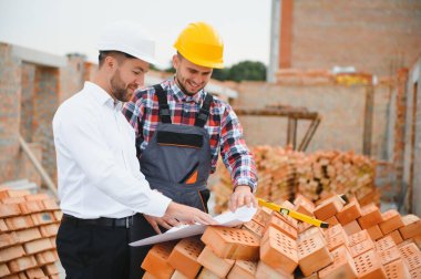 Başlık ve güvenlik yeleği giyen mühendis büyük inşaat alanında takım halinde çalışıyor..