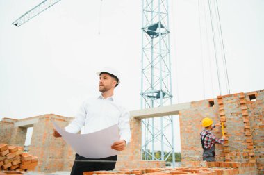 İnşaat alanındaki Mühendislik Danışmanlığı elinde planları tutuyor. İnşaat müfettişi. Yeni binanın inşaat sahası çizimi ve iş akışı