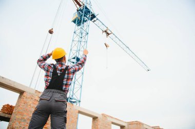 Sarı renkli başlık. Gündüz vakti inşaatta üniformalı genç bir adam çalışıyor.