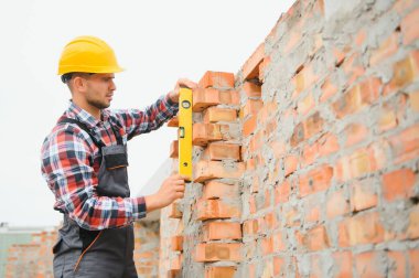 Sarı renkli başlık. Gündüz vakti inşaatta üniformalı genç bir adam çalışıyor.