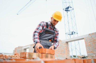 Tuğla duvarla meşgul. Üniformalı inşaat işçisi ve güvenlik ekipmanı inşaatında çalışıyor