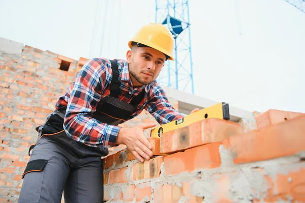 Construction worker man in work clothes and a construction helmet. Portrait of positive male builder in hardhat working at construction site