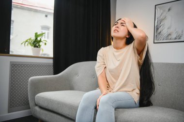 Kız başını tutuyor, kadının başı ağrıyor. Üzgün kadın kanepede oturuyor..