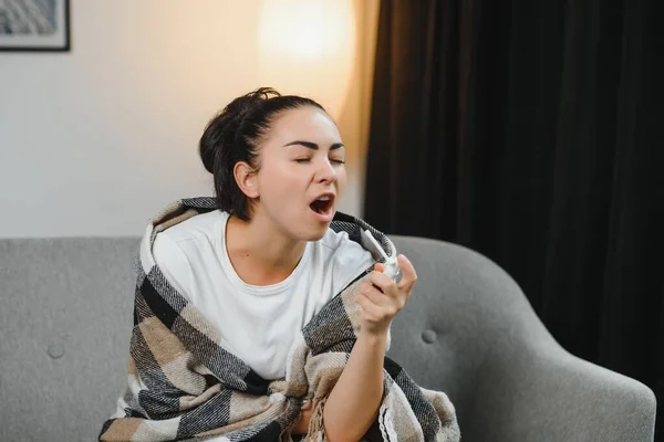 sick young woman in scarf using cough spray