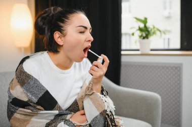 Sağlık, soğuk algınlığı ve insanlar konsepti - üzgün, hasta, genç kadın evde ağız spreyi kullanıyor..