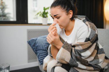 Hasta bir kadın evde kanepede oturan bir baş ağrısı ile gri battaniyeye sarılmış.