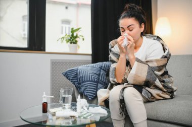 Hasta bir kadın evde kanepede oturan bir baş ağrısı ile gri battaniyeye sarılmış.