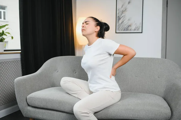 背中の痛みのために不快感を感じ リビングルームでソファに座っている不幸なシニアブロンド 腰痛に苦しんで成熟した女性を動揺 — ストック写真