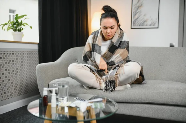 Hasta kadın. Flu. kadın üşüttü. Dokuların içine hapşırmak. Baş ağrısı. Virüs. İlaçlar. Kanepede oturan, başı ağrıyan hasta kadın.