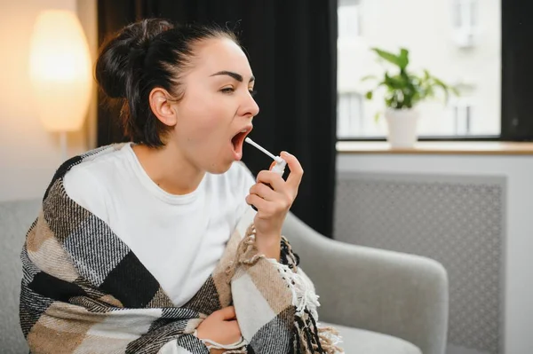 Sağlık, soğuk algınlığı ve insanlar konsepti - üzgün, hasta, genç kadın evde ağız spreyi kullanıyor..