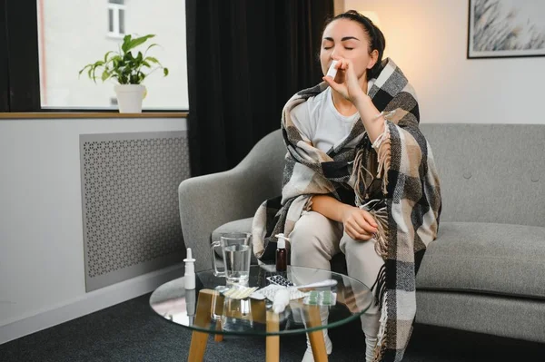 Kanepede oturan hasta genç bir kadının burun spreyi. Alerjik rhinitis semptomlar ve tedavi.