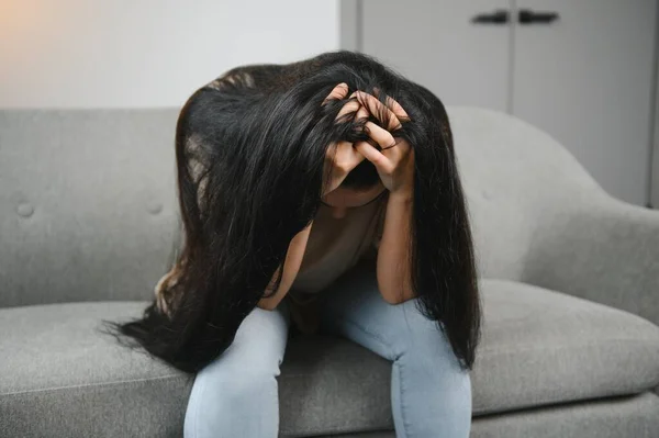 Depressed sad attractive woman crying on sofa couch at home feeling lonely tired and worried suffering depression in mental health, loneliness and isolation concept. Psychology, solitude and people