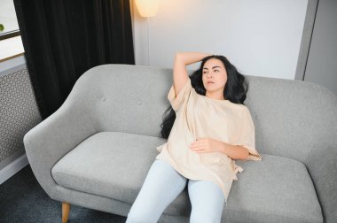 Güzel İspanyol bir kadın, acı dolu bir ifadeyle karnını tutuyor. Adet sancısı çekiyor. Evde üzgün yatıyor, kadın sağlığı konseptinde karnı ağrıyor..