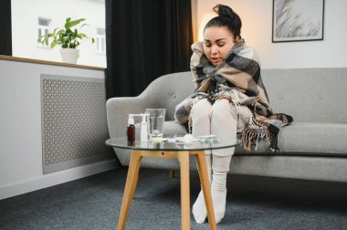 Hasta kadın. Flu. kadın üşüttü. Dokuların içine hapşırmak. Baş ağrısı. Virüs. İlaçlar. Kanepede oturan, başı ağrıyan hasta kadın.