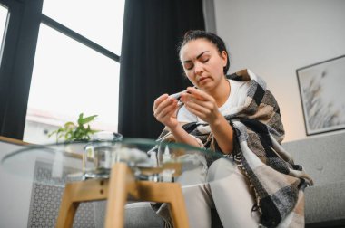 Hasta bir kadın evde kanepede oturan bir baş ağrısı ile gri battaniyeye sarılmış.