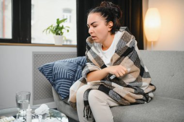 Hasta bir kadın evde kanepede oturan bir baş ağrısı ile gri battaniyeye sarılmış.