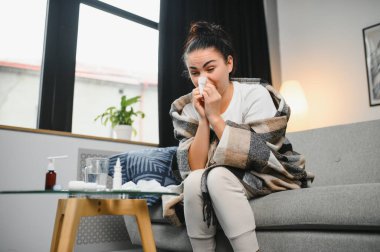 Hasta bir kadın evde kanepede oturan bir baş ağrısı ile gri battaniyeye sarılmış.