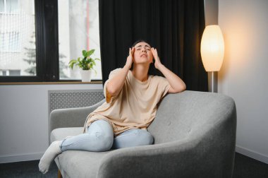 Kafasına dokunan yorgun bir kız, baş ağrısı, migren, evdeki kanepede oturmak. Depresyondaki genç kadın kayıp, keder ve travmayla baş ediyor. Sinir krizi, kriz konsepti