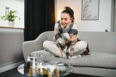 Hasta bir kadın evde kanepede oturan bir baş ağrısı ile gri battaniyeye sarılmış.