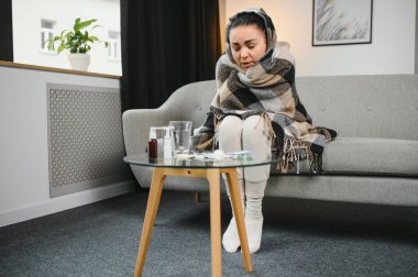 Hasta bir kadın evde kanepede oturan bir baş ağrısı ile gri battaniyeye sarılmış.