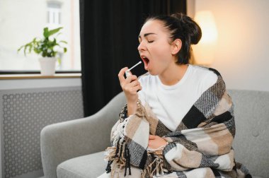 Sağlık, soğuk algınlığı ve insanlar konsepti - üzgün, hasta, genç kadın evde ağız spreyi kullanıyor..