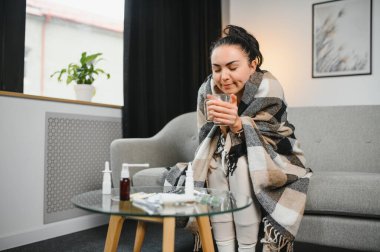 Hasta bir kadın evde kanepede oturan bir baş ağrısı ile gri battaniyeye sarılmış.