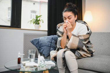 Genç bir kadın kanepeye oturur, battaniyeyle kaplanır, donar, burnunu siler, mendile hapşırır. Kadın ateşlendi, grip oldu ve grip belirtileri evde öksürüyor. Solunum hastalığına alerjim var..