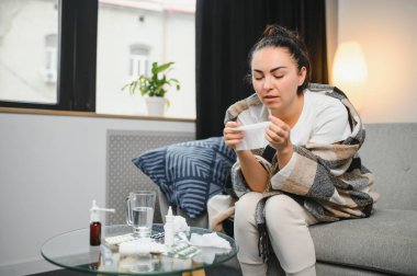 Genç bir kadın kanepeye oturur, battaniyeyle kaplanır, donar, burnunu siler, mendile hapşırır. Kadın ateşlendi, grip oldu ve grip belirtileri evde öksürüyor. Solunum hastalığına alerjim var..