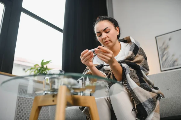 Hasta bir kadın evde kanepede oturan bir baş ağrısı ile gri battaniyeye sarılmış.