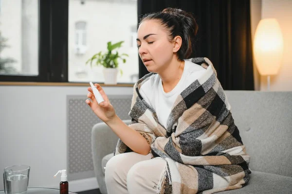 坐在沙发上的生病的年轻女人手里拿着鼻涕喷雾 过敏性鼻炎的症状和治疗 — 图库照片
