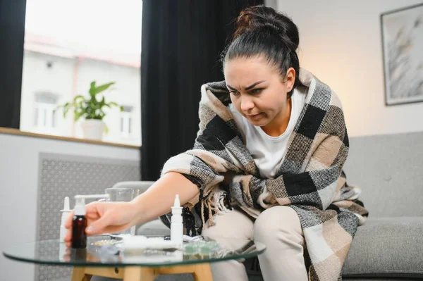 Hasta bir kadın evde kanepede oturan bir baş ağrısı ile gri battaniyeye sarılmış.