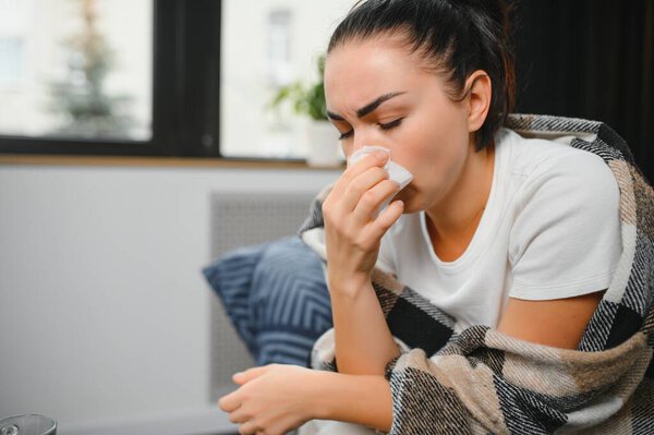 healthcare, cold, allergy and people concept - sick woman blowing her runny nose in paper tissue at home
