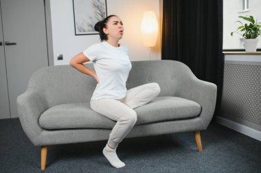 Üzgün genç kadın sırtına dokunuyor sırtı ağrıyor sabah rahatsızlığı bel kası ağrısı uyandıktan sonra yatağa oturuyor..