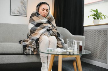 Hasta kadın. Flu. kadın üşüttü. Dokuların içine hapşırmak. Baş ağrısı. Virüs. İlaçlar. Kanepede oturan, başı ağrıyan hasta kadın.