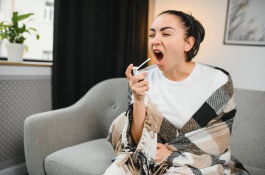 Sağlık, soğuk algınlığı ve insanlar konsepti - üzgün, hasta, genç kadın evde ağız spreyi kullanıyor..