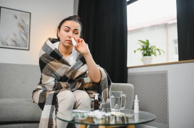 Kanepede oturan hasta genç bir kadının burun spreyi. Alerjik rhinitis semptomlar ve tedavi.