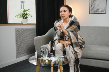 Kanepede oturan hasta genç bir kadının burun spreyi. Alerjik rhinitis semptomlar ve tedavi.