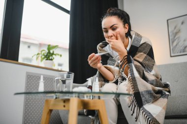 Hasta bir kadın evde kanepede oturan bir baş ağrısı ile gri battaniyeye sarılmış.