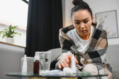 Hasta bir kadın evde kanepede oturan bir baş ağrısı ile gri battaniyeye sarılmış.